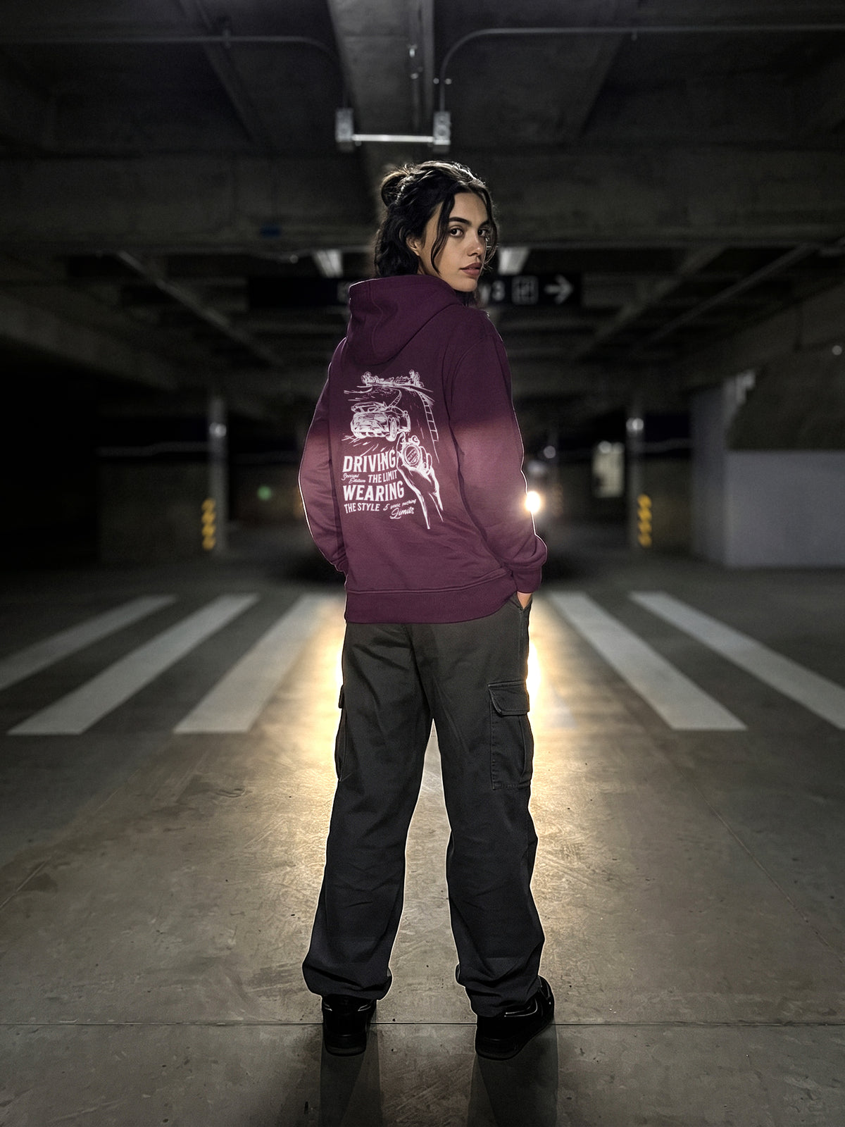 Modell trägt den Driving the Limit Hoodie in Plum mit weißem Siebdruck auf dem Rücken
